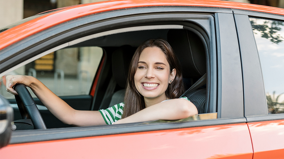 Happy millennial middle aged woman driving an orange car wearing a green striped t-shirt